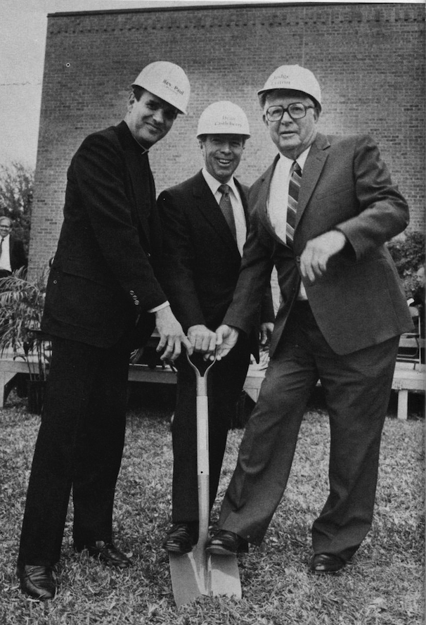 Three Men in suites wearing white hard hats, sharing a short shovel on a part of the StMU Lawn for the Law Library | Fr. Dave Paul on left, Dean Castleberry in Center, Judge Lytton on right.